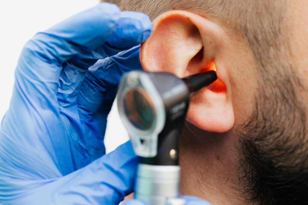 Nahaufnahme eines Arztes, der in einer klinischen Umgebung mit einem Otoskop das Ohr eines Patienten untersucht.